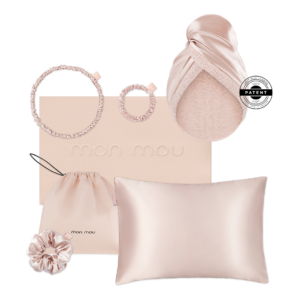 Blush satin hair accessories and a pillow on a pale pink Mon Mou box, including two scrunchies, a drawstring pouch, and a head wrap.