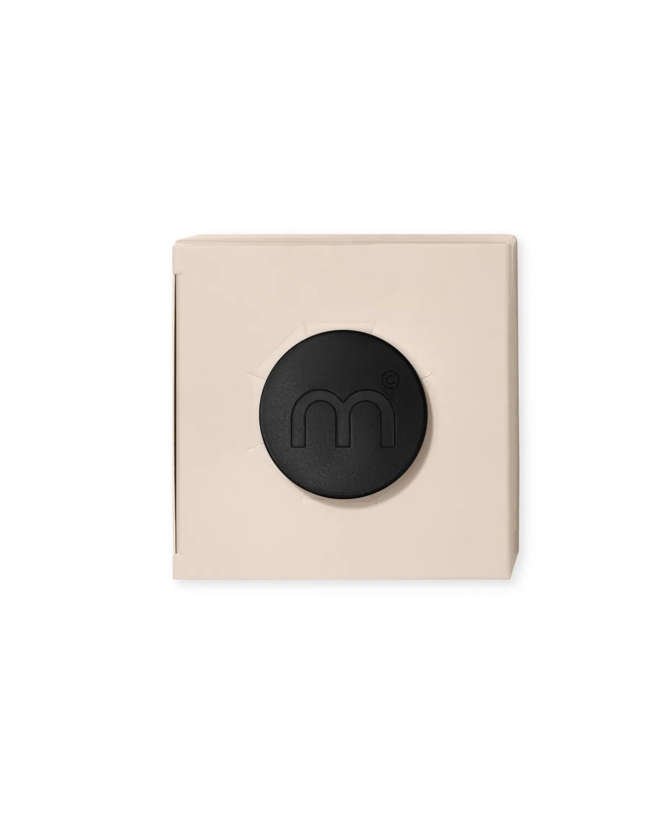 Beige square box with a large black circular emblem featuring a stylized 'm' on its center-right area (close-up).