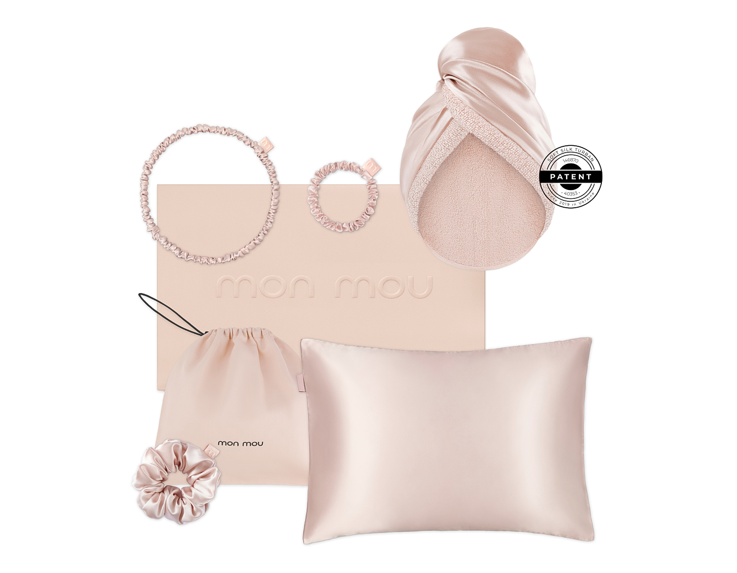 Blush satin hair accessories and a pillow on a pale pink Mon Mou box, including two scrunchies, a drawstring pouch, and a head wrap.
