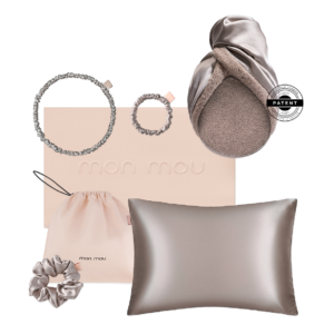 Flat lay of blush-pink fashion set: satin pillow, drawstring pouch, two textured rings and a scrunchie with a metallic box logo in soft tones.