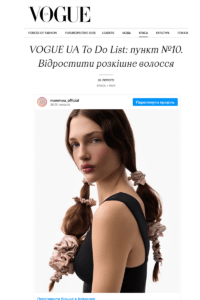 Model with long brown hair in two side ponytails tied with pink scrunchies, wearing a black sleeveless top, white background