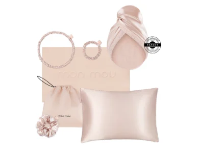 Flat lay of pastel pink satin accessories: two scrunchies, a drawstring pouch, a pillow, and a blush box labeled 'mon mou'.