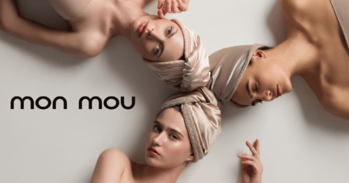 Four women wearing beige head wraps lie on a pale surface in a circle, with the brand name 'mon mou' shown in the bottom-left corner.