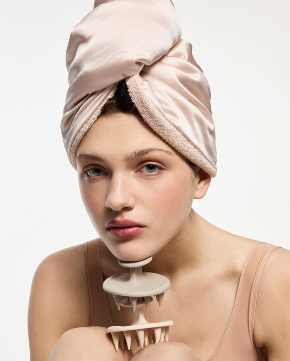 Woman with a soft pink towel wrapped around her head, holding a beige spiked jaw exercise device near her chin.