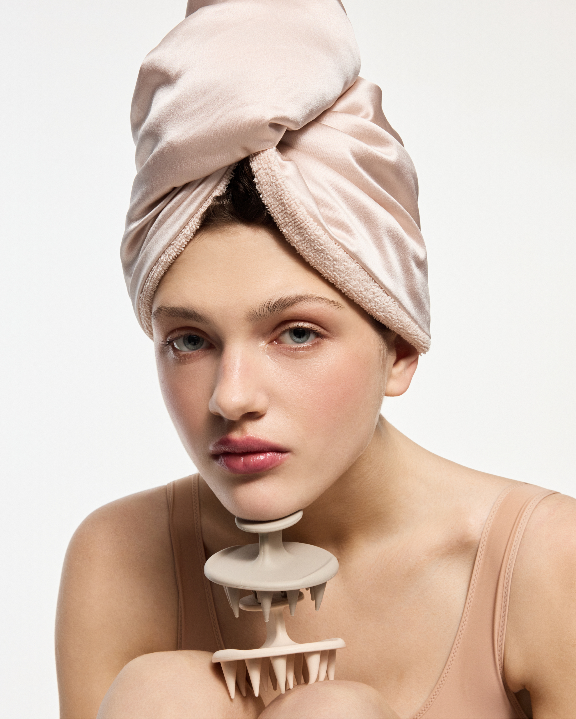 Woman with a soft pink towel wrapped around her head, holding a beige spiked jaw exercise device near her chin.