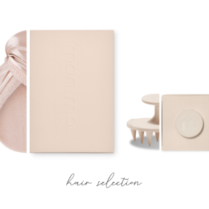 Flat lay of pale pink beauty products on a white background: towel, boxed items, and a small grooming tool, all in soft pastel tones.