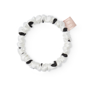 White satin scrunchie with black leopard spots, laid in a loose circle on a white background (close-up).