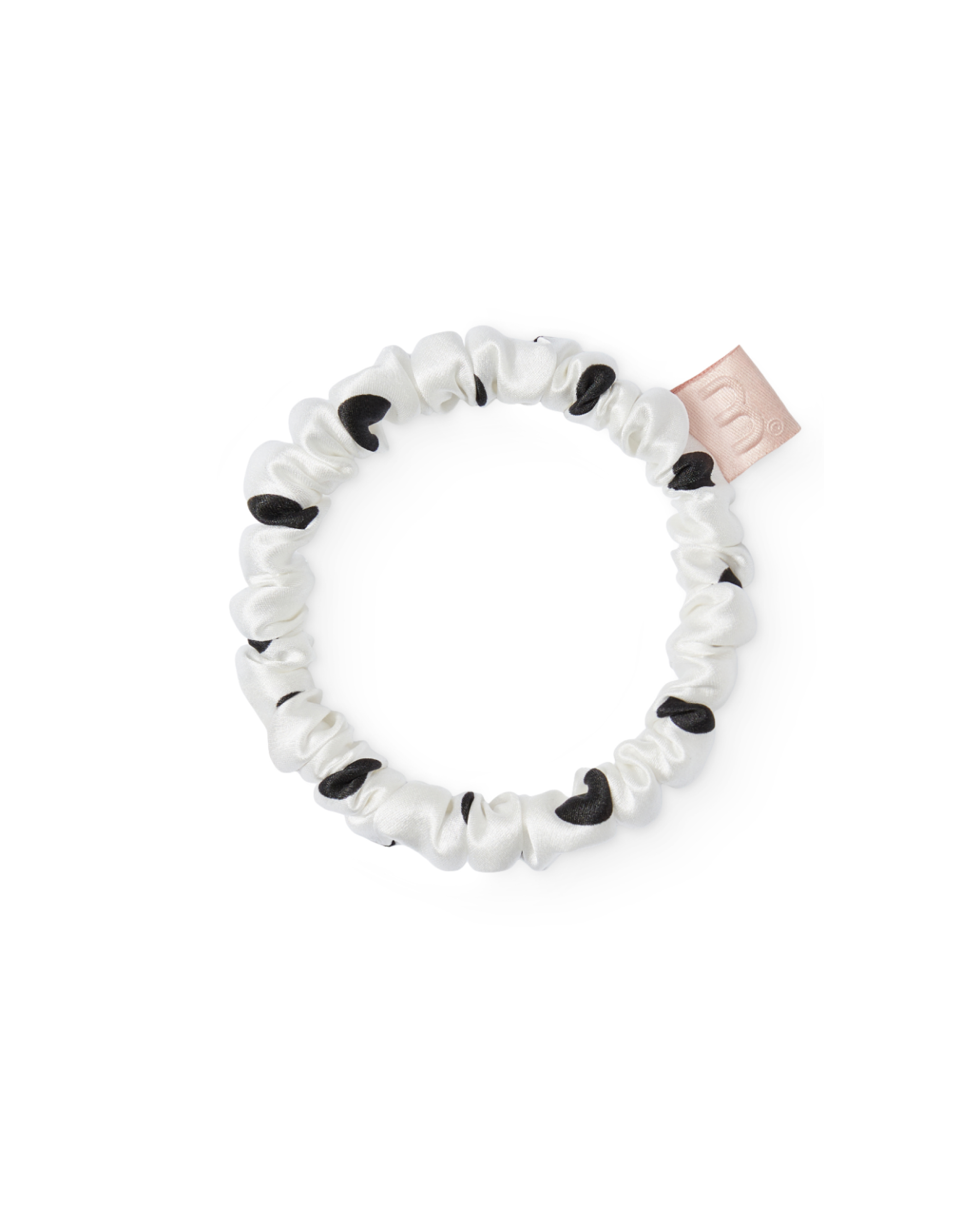 White satin scrunchie with black polka dots and a pale pink brand tag, shown in a close-up.