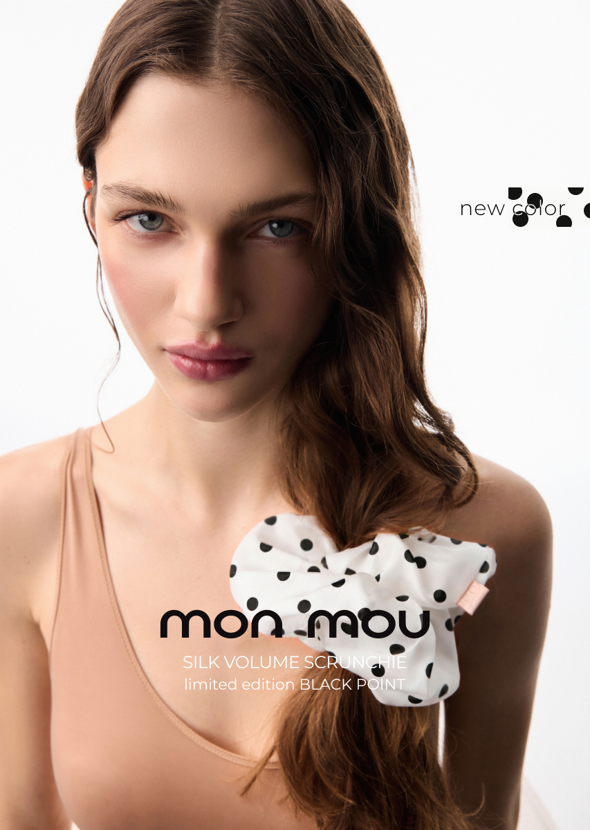 Close-up of a woman with long brown hair wearing a beige top and a white polka-dot silk scrunchie, in a Mon Mou fashion ad (new color).