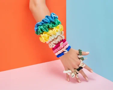 Colorful fabric scrunchies wrapped around a forearm and hand against a bright orange and blue split background