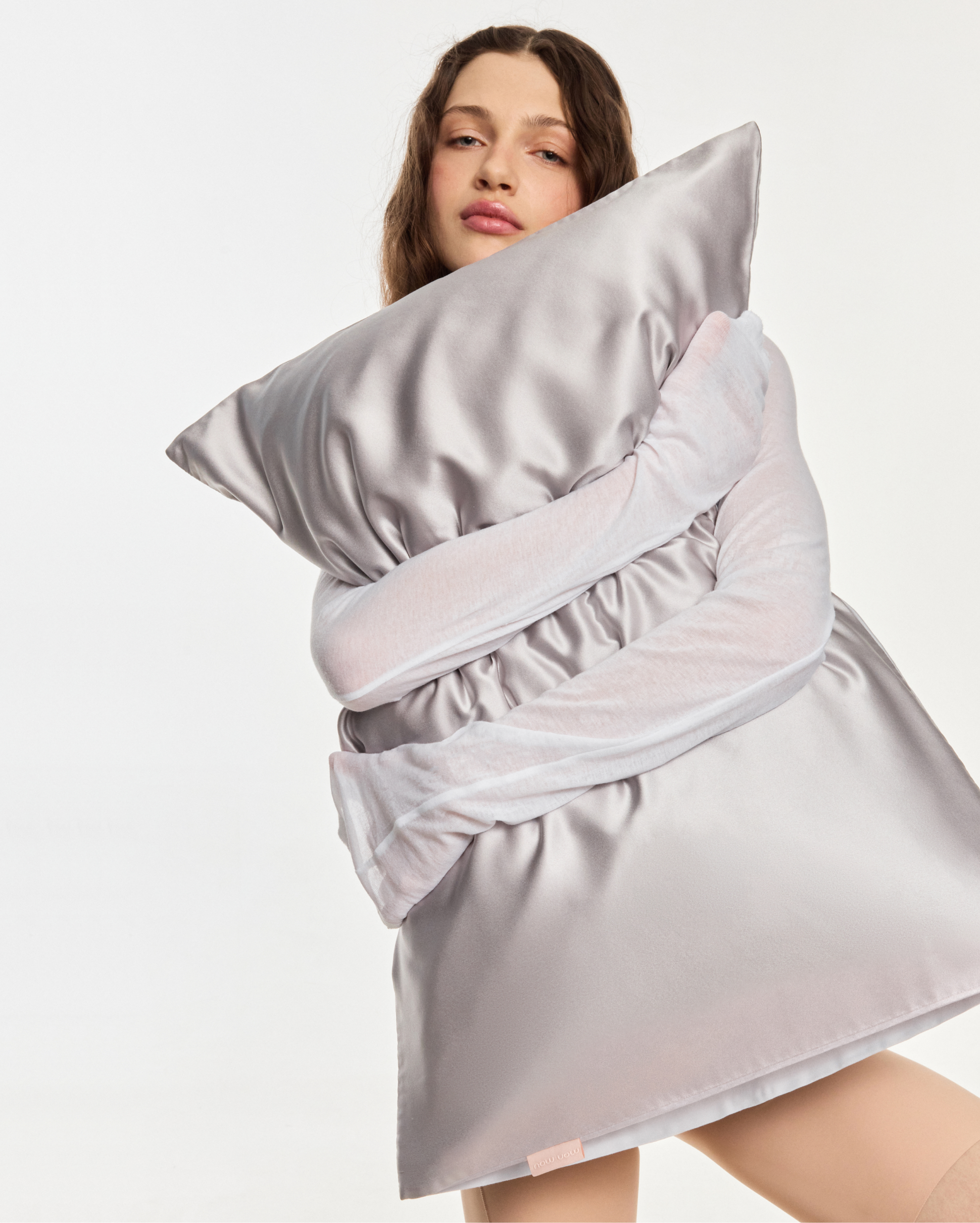 Person wrapped in a large pale pink satin blanket draped over shoulders, posing against a light background.