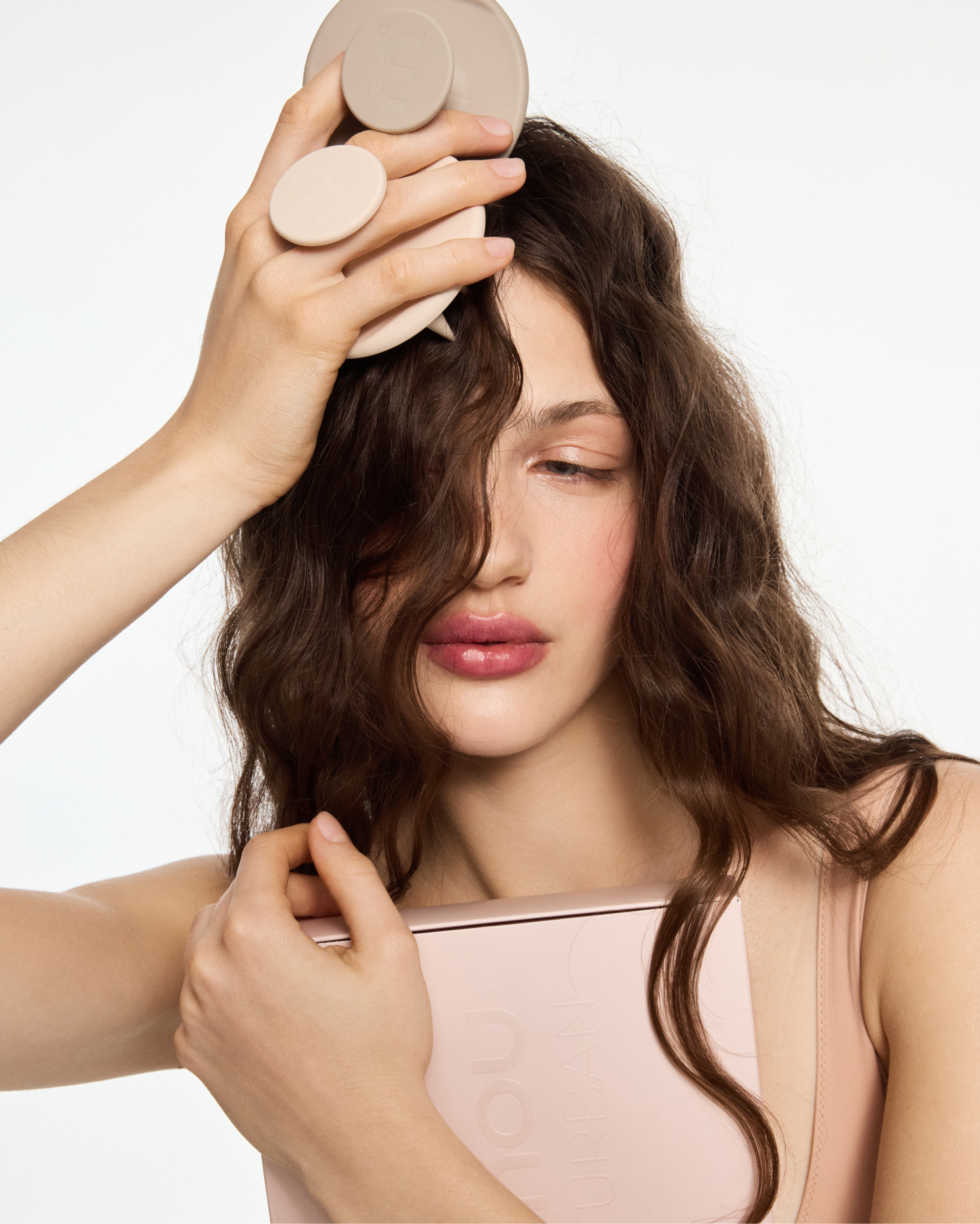 Woman with long brown hair holding a round beige beauty device against her scalp.