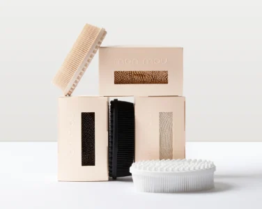 Stack of pale beige boxes with textured inserts and a large ribbed circular object leaning against them.