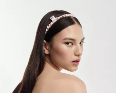 Close-up of a woman wearing a pale pink satin ruched headband in her dark hair, viewed from the side