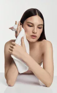 Woman with long dark hair drying her face with a white towel in a studio setting