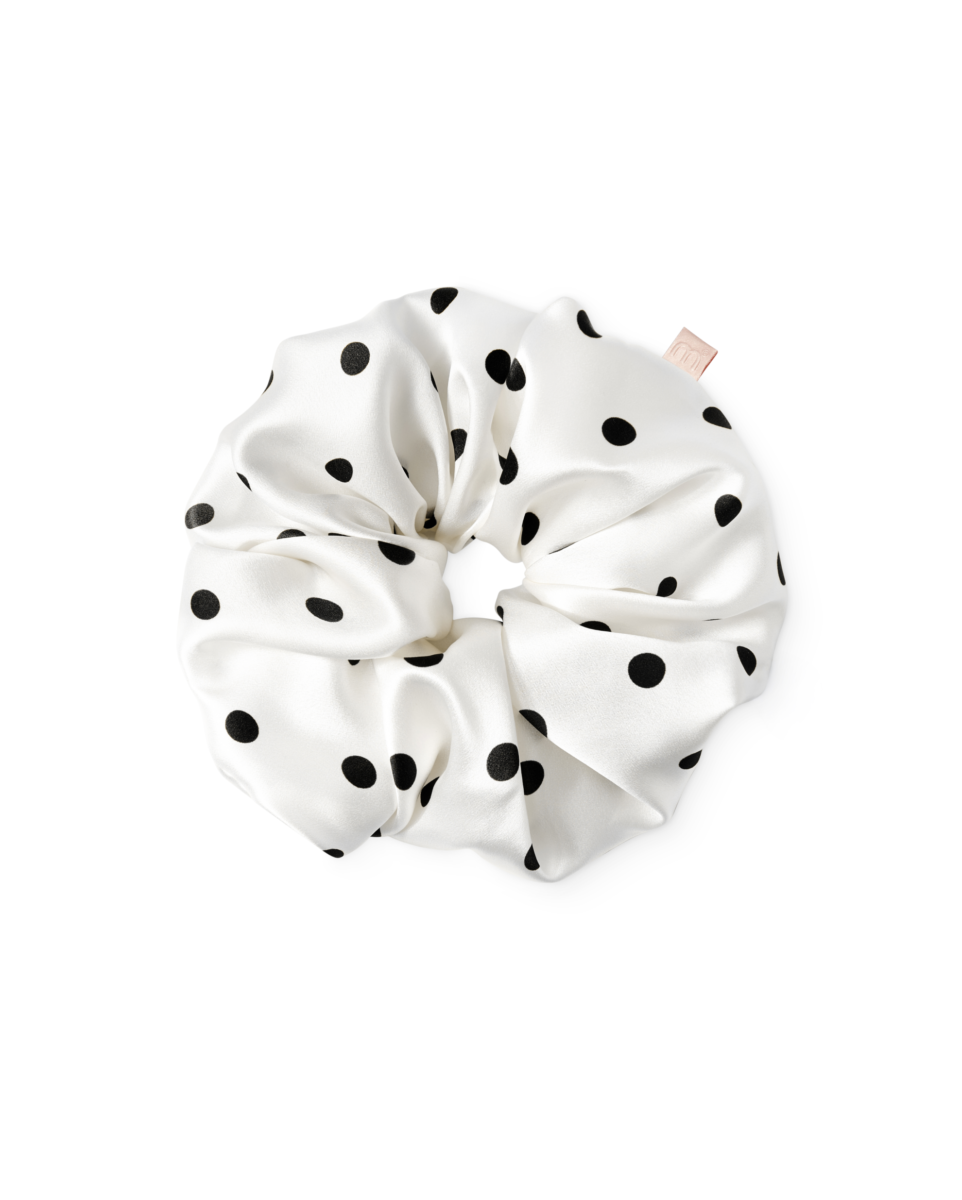 White satin hair scrunchie with black polka dots, gathered in a circular shape against a white background.