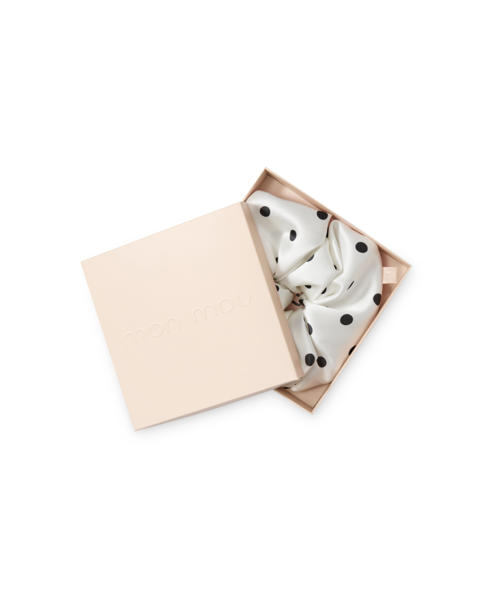 Open blush-pink gift box with a white satin scarf featuring black polka dots spilling out of the lid.