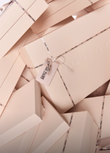 Many white gift boxes wrapped with white ribbons, stacked in a pile with ribbons that read 'mon mou'.