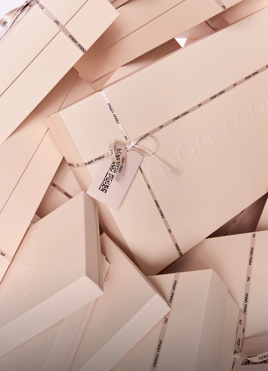 Pile of pale beige gift boxes wrapped with white ribbons and "mon mou" branding on the ribbons.