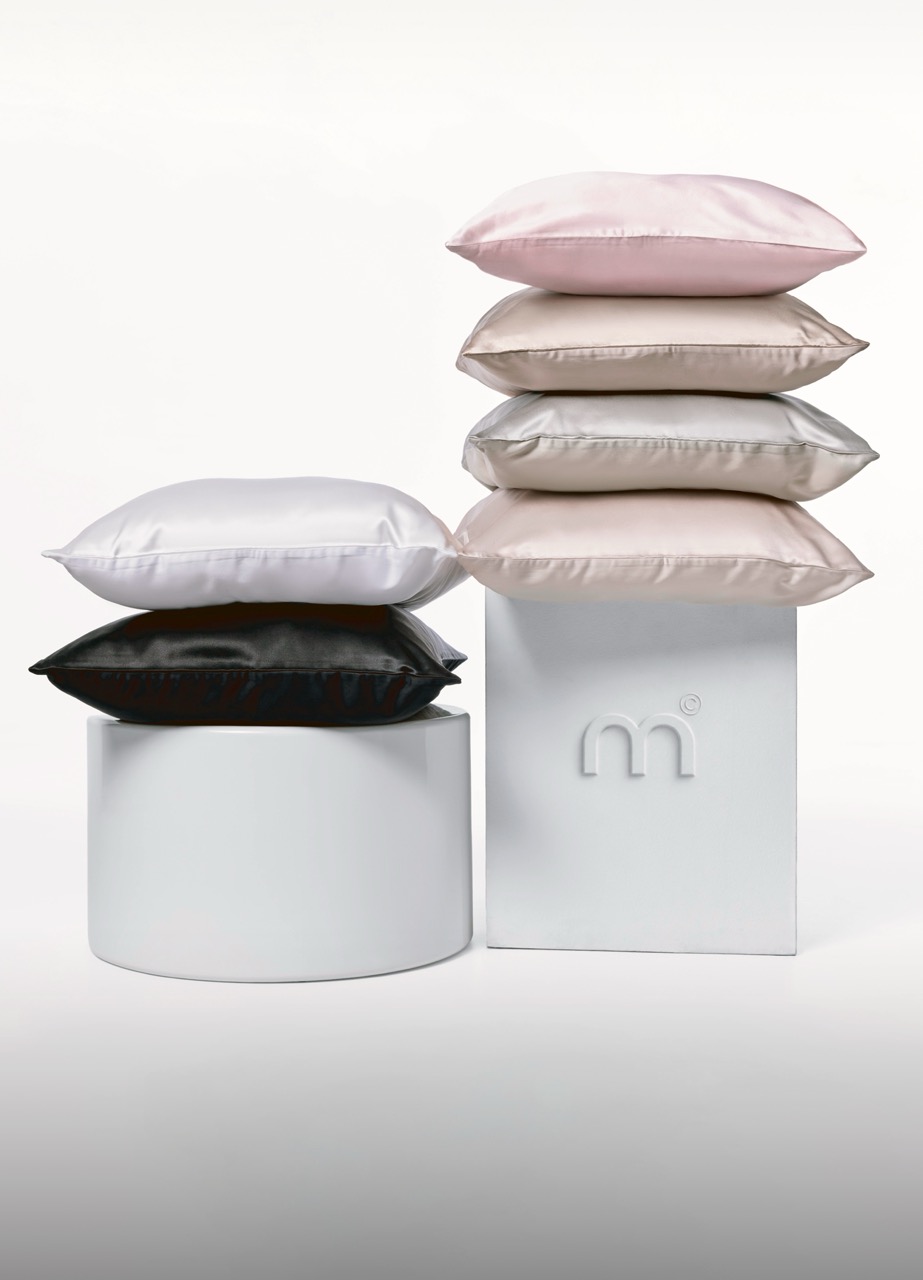Stack of satin pillows in pink, beige, and white on white display stands, forming a studio product shot.