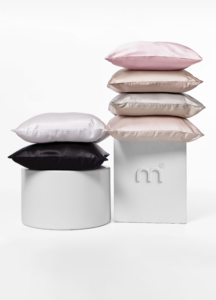 Stack of satin throw pillows in pale pink, beige, and black on white display stands.