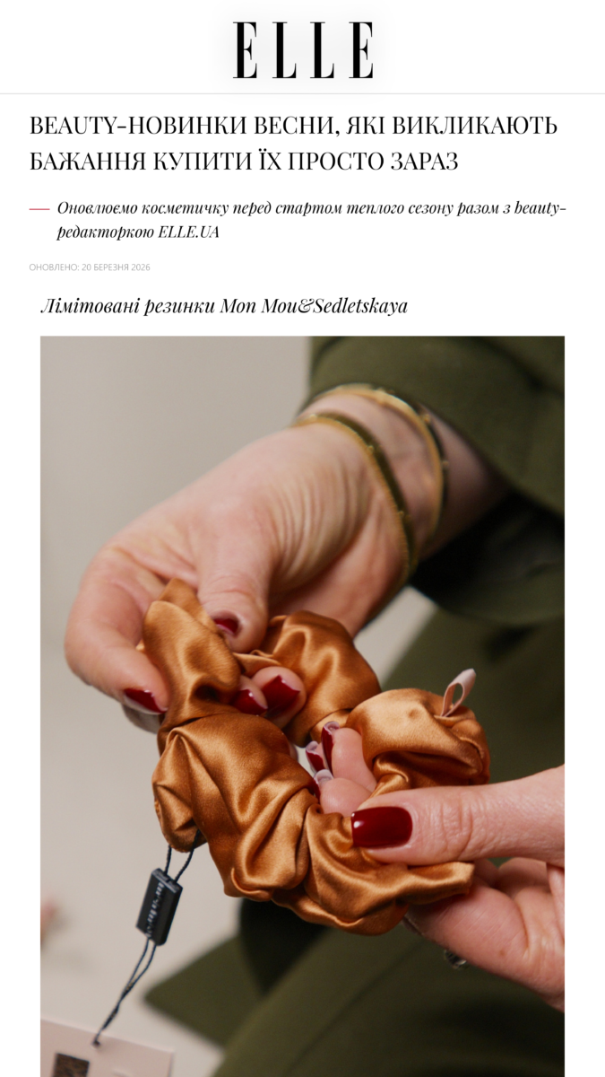 Close-up of hands holding a brown satin scrunchie with a hair tie and tag visible.