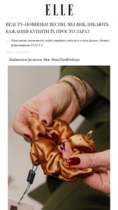 Close-up of hands twisting a bronze-satin hair scrunchie, with a small tag visible on a cord nearby.