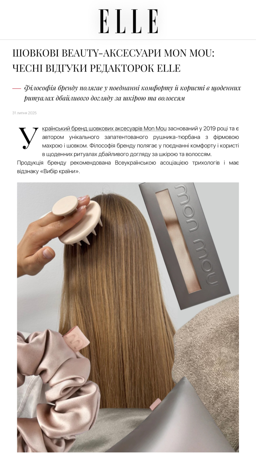 Hand brushing long brown hair with a beige round brush; a straightener sits nearby in the background.