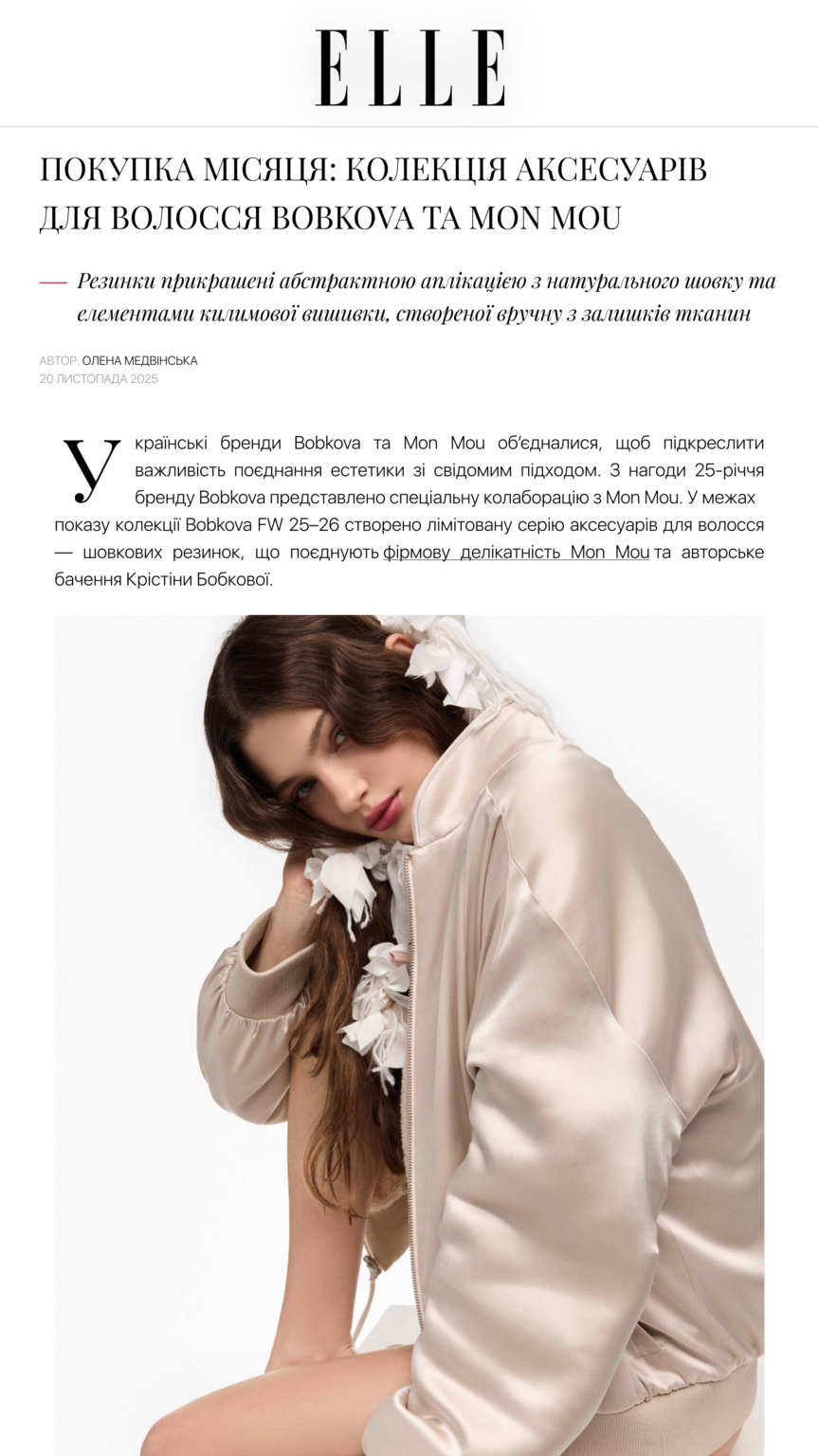Model wearing a beige satin bomber jacket with white flower embellishments, posing in a studio.