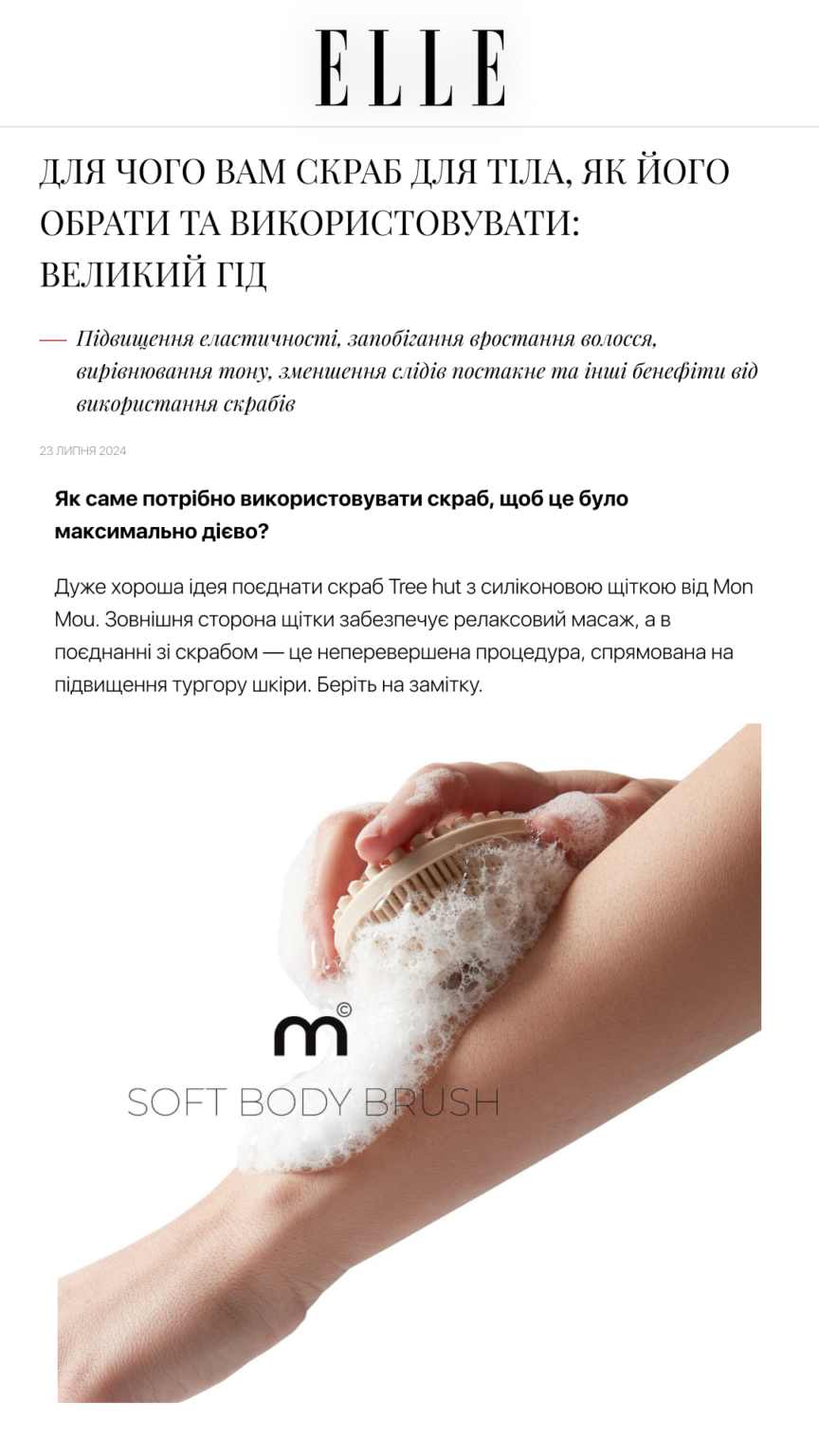 Close-up of a hand using a soft body brush with soapy lather on the skin, in an Elle article about body scrubs (Ukraine). The brush is labeled Soft Body Brush in the image.